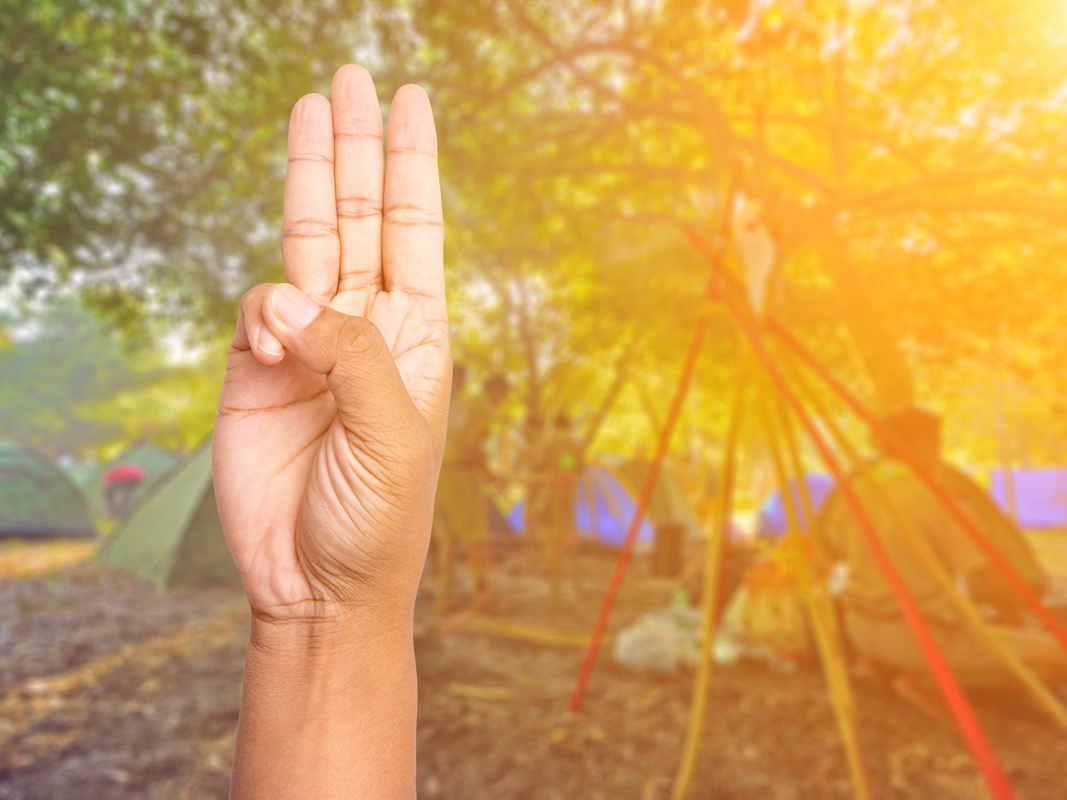 Scout honor hand gesture on blurred scouts camping background.